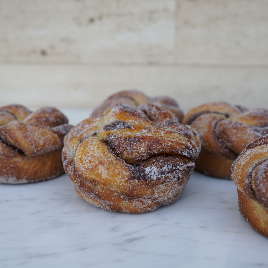 A close-up image of a cinnamon brioche bun, sprinkled with sugar, showing the soft, fluffy texture and the cinnamon spice.