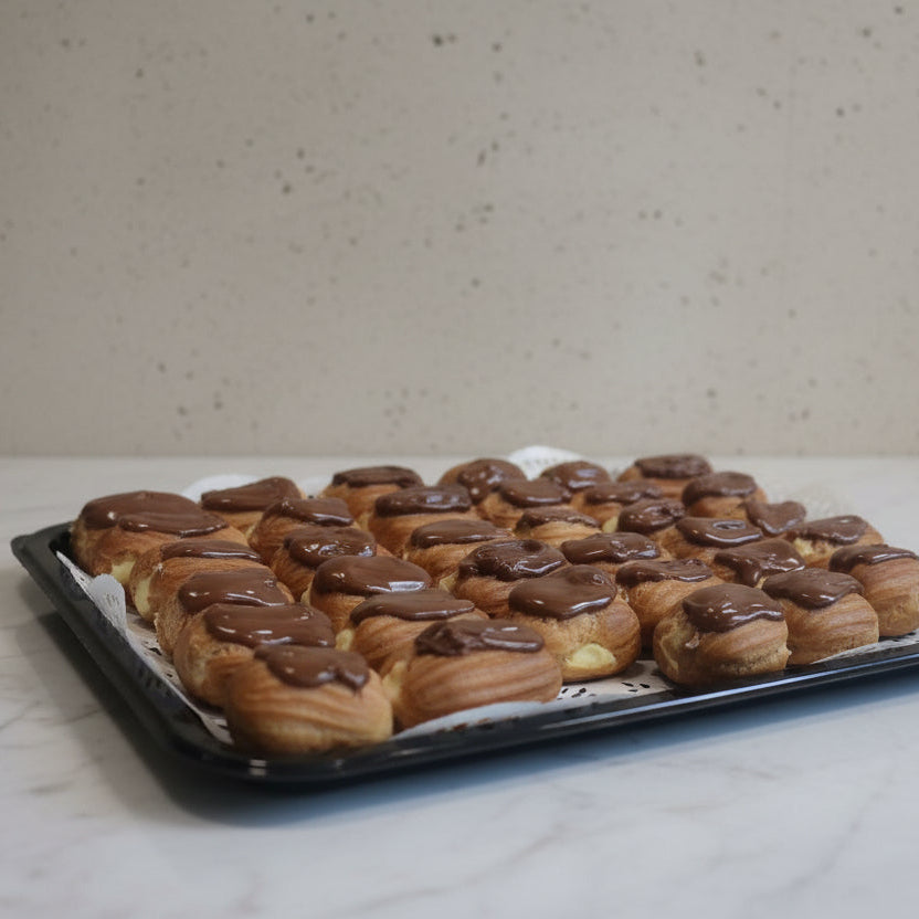 A tray of mini eclairs canapes arranged on a white paper doily over a black baking tray, in North London.