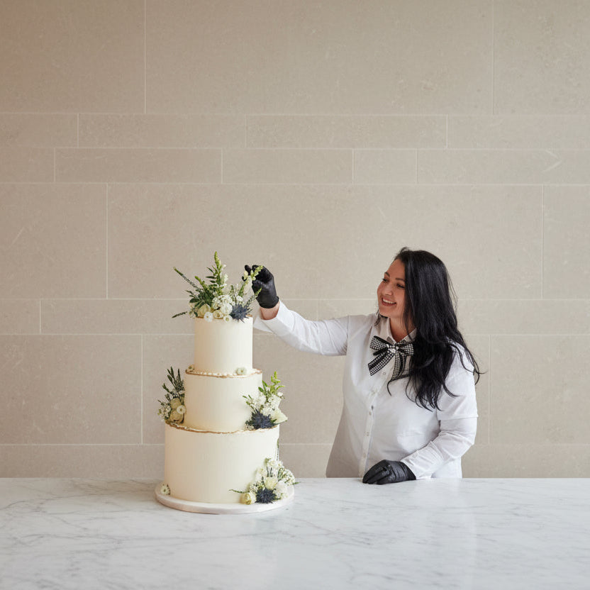 Geanina finishing a wedding cake in front of a window with a teal frame.